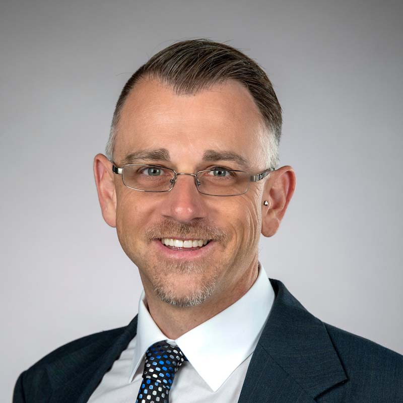 Headshot of Jason Rohr, wearing a suit, tie and glasses.