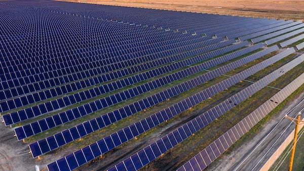 An aerial view of a large solar panel farm with thousands of panels stretching out into the distance.