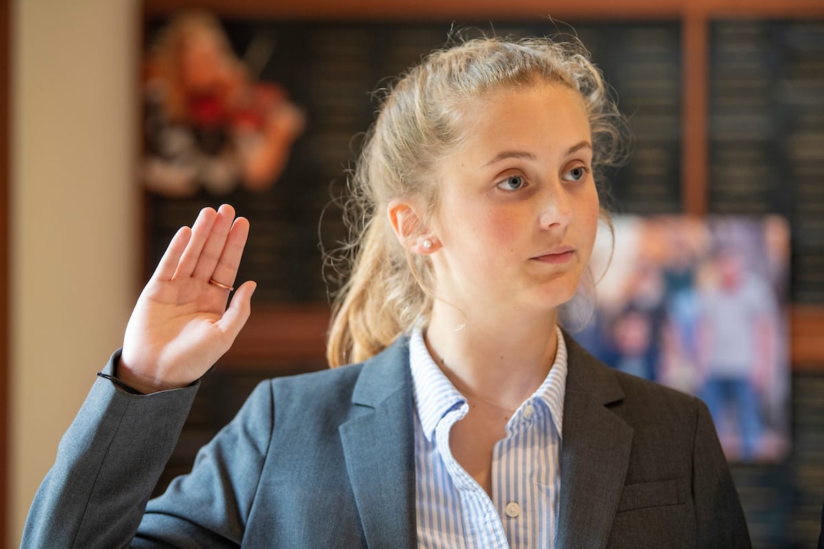 A female student holds her hand up while being sworn in.