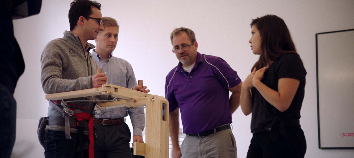 Marissa and teammates stand with wooden prototype of her walker.