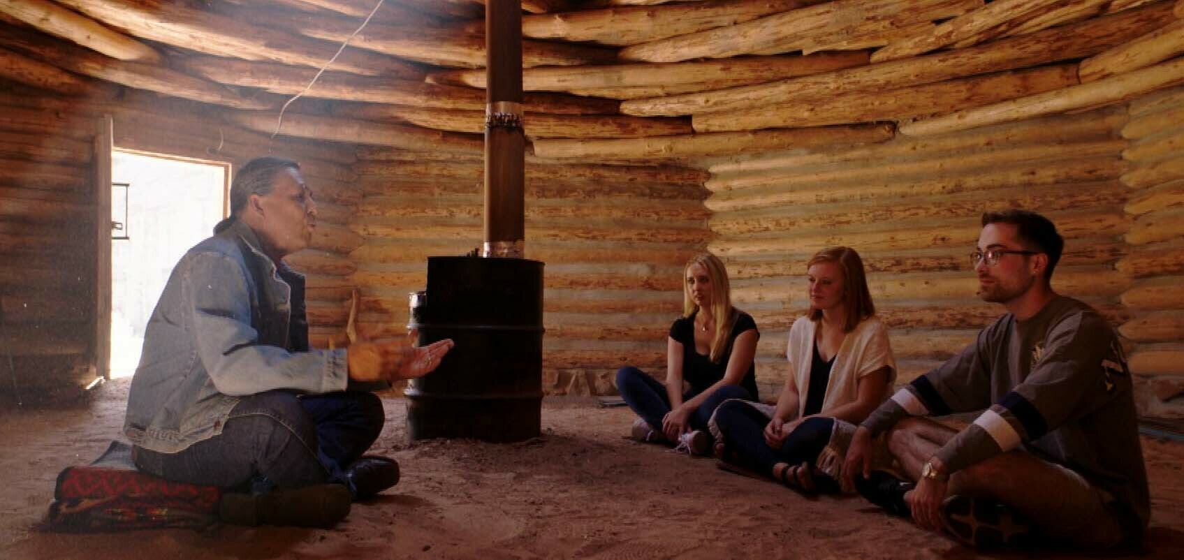 Three students and a man sit inside a curved wooden building.