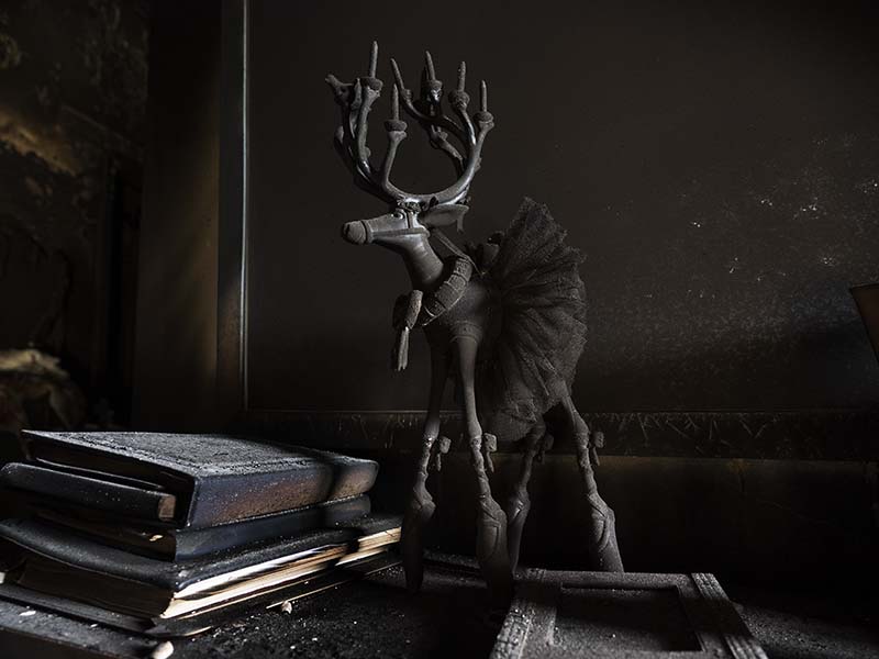 A reindeer statue wearing a tutu on a desk with books, all covered with black ash.
