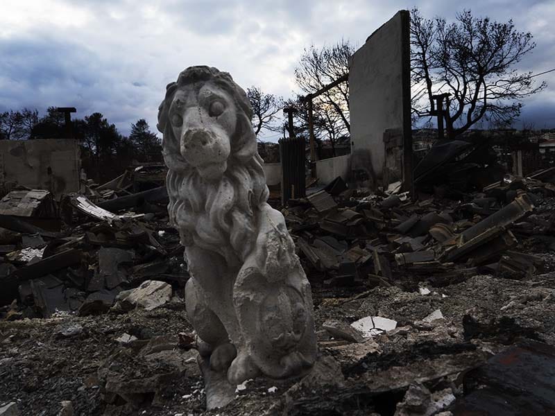 A gargoyle stands among burned debris.