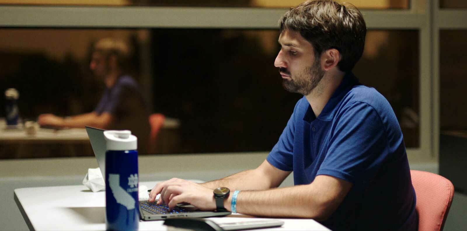 Evan Nichols types on a laptop at a desk.