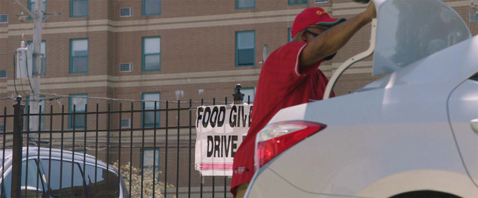 A man closes a car trunk in front of a food drive sign.
