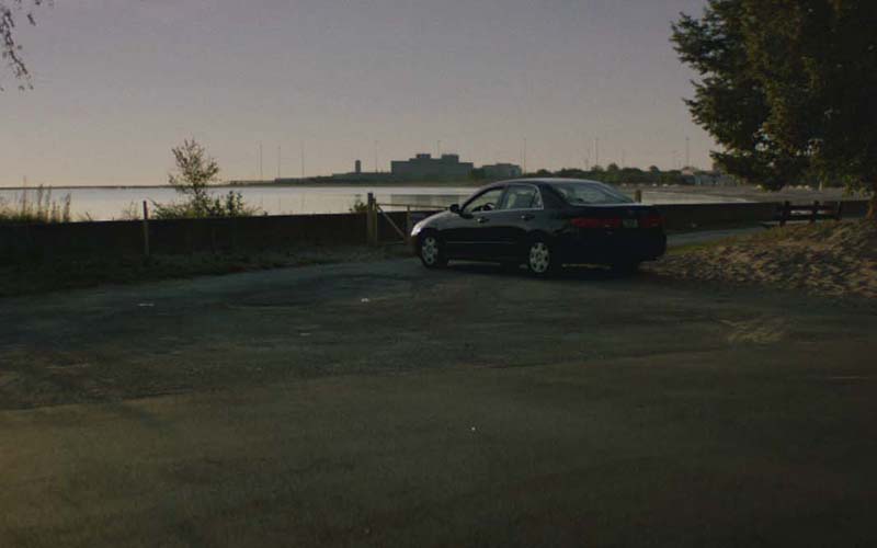 A lone car parked in a lot by the lake.