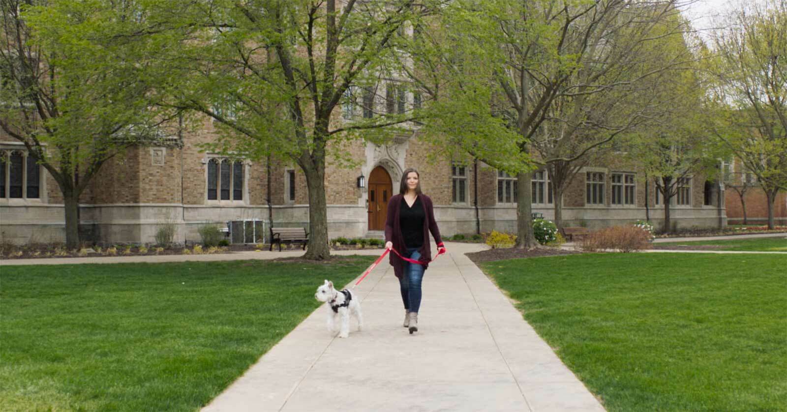A woman walking a dog on a sidewalk.
