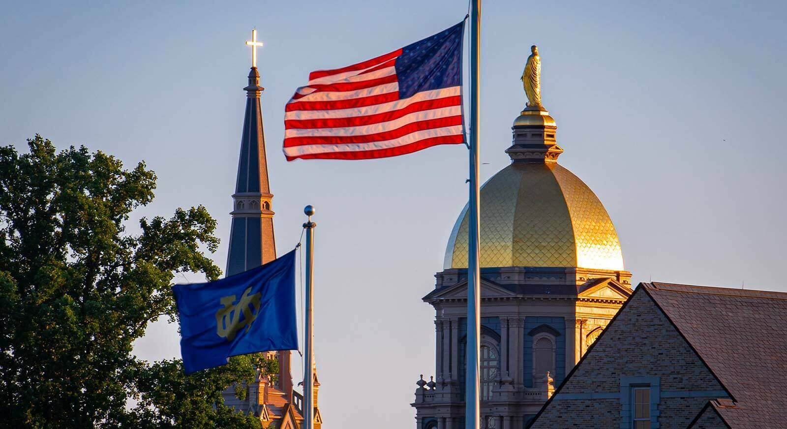 The U.S. flag along with an ND flag fly in front of the Golden Dome and Basilica during the afternoon.
