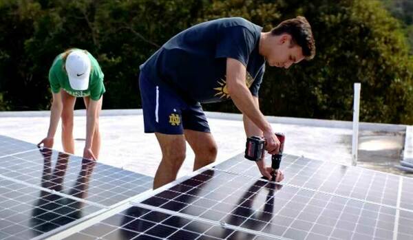 A male student uses a drill to install a solar panel.