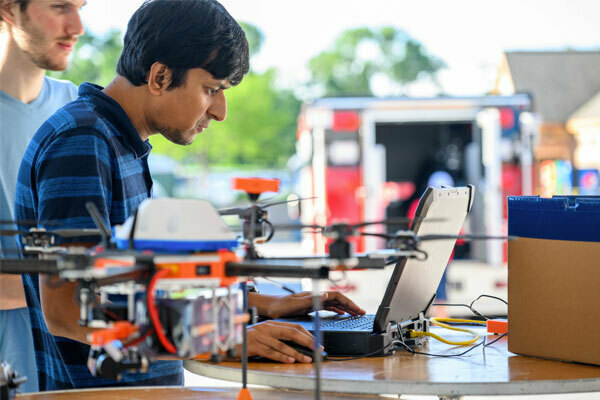 A student works on his computer next to a drone.