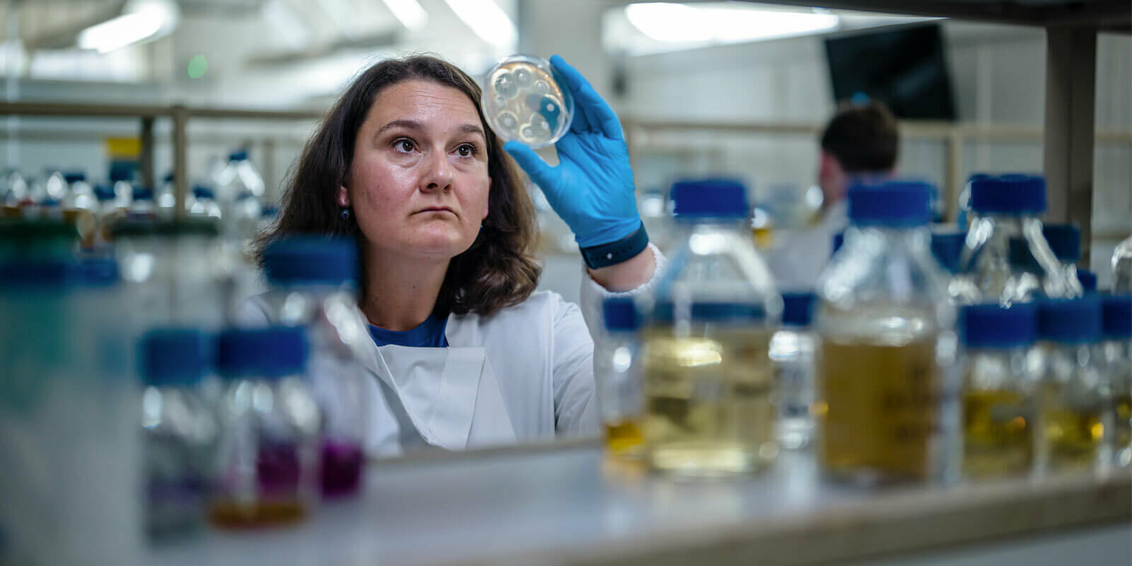 Martha Martins in her lab coat looking at a petri dish she's holding up.