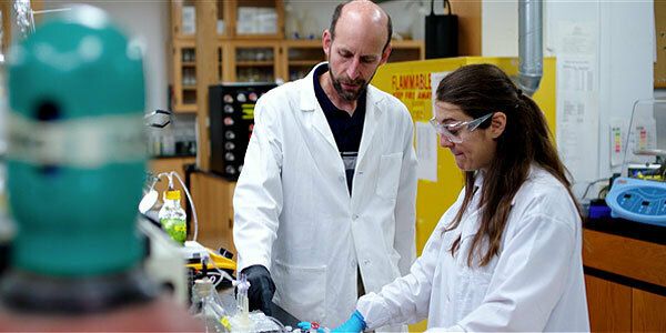 A male and female in lab coats looking at capped test tubes.