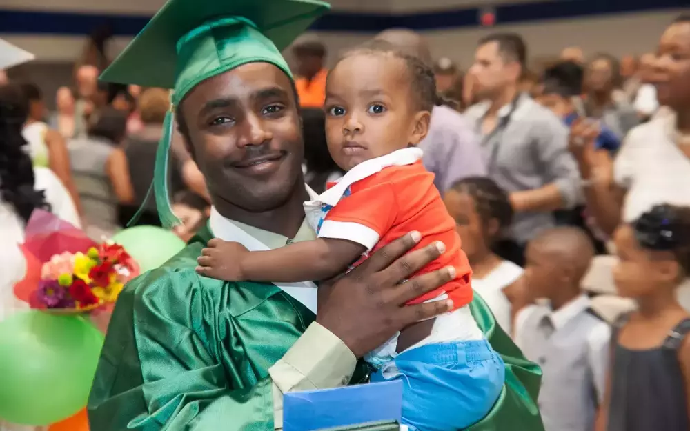 Man wearing a cap and gown smiling while holding a toddler.