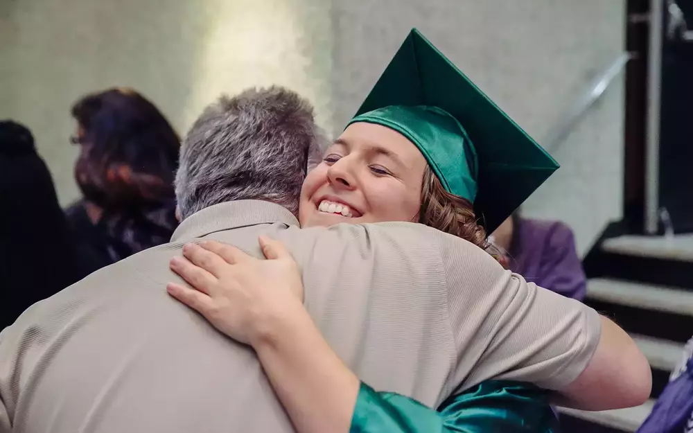 Woman in graduation cap and gown hugging a man.