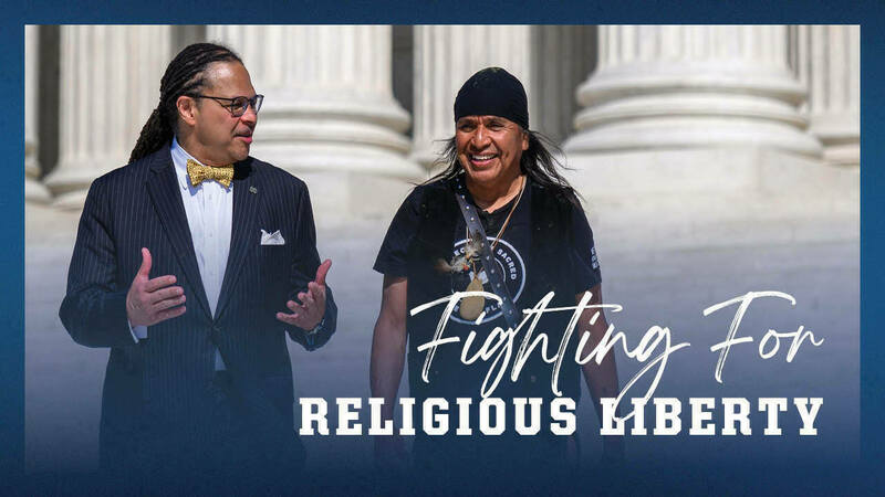 A black man and a Native American man walk and talk in front of a building with large columns. Text overlaid on the image reads &quot;Fighting For Religious Liberty&quot;.