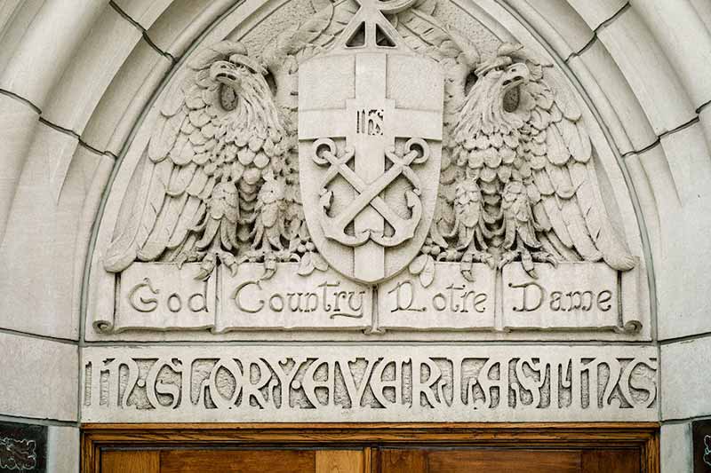 A stone carving above a doorway with the words, ‘God, Country, Notre Dame&rsquoi; flanked by two eagle-like figures. 