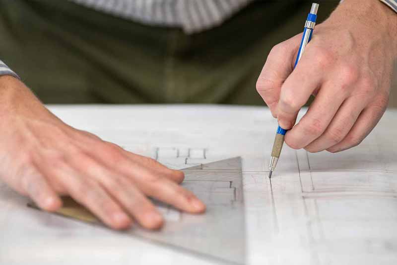 A person's hands work on a blueprint with a pencil and a ruler, drawing lines. 