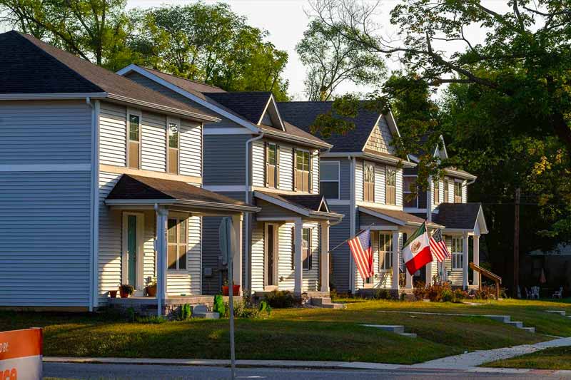 A row of three duplex houses with porch columns and American, Italian, and Mexican flags displayed in front. 