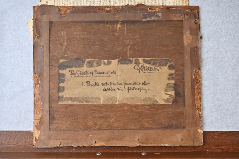 Wooden back of a framed picture with a partial label reading The Ghosts of Beaconsfield. and I. Burke rebukes the journalist who dabbles in philosophy.  A signature is visible above the text.
