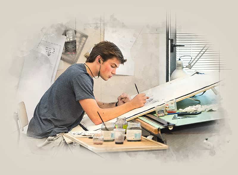 A young man wearing headphones sits in a chair sketching on a table, paint cups and tools in the foreground.