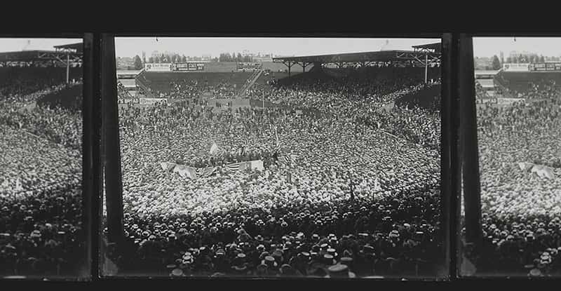 Three black-and-white film frames show a large crowd gathered in a stadium with stands and buildings in the background.