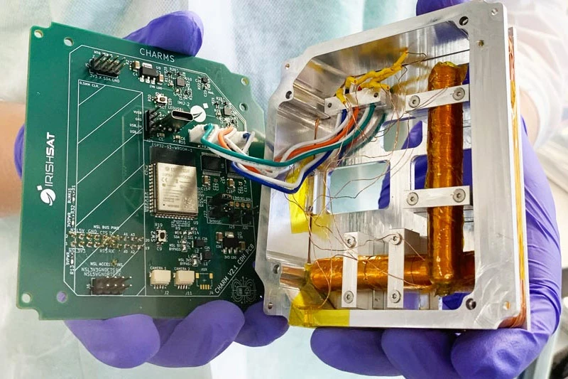 Purple gloved hands hold components of a mini satellite