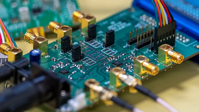 A green circuit board featuring multiple gold SMA connectors, a multi-colored ribbon cable plugged into a header, and black cables attached to other connectors.